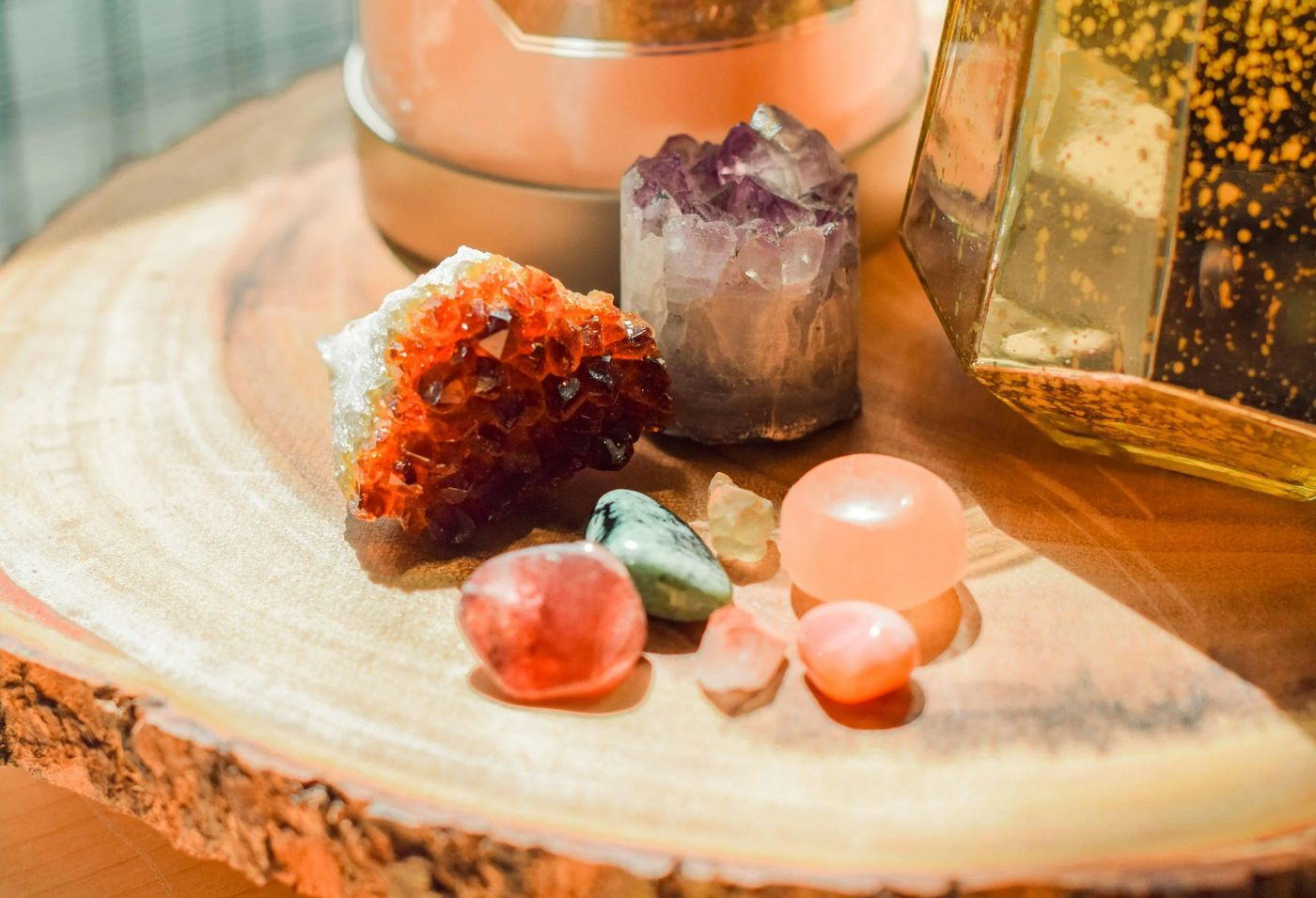 Crystals and tumbled stones on a wood slice beside a glowing salt lamp