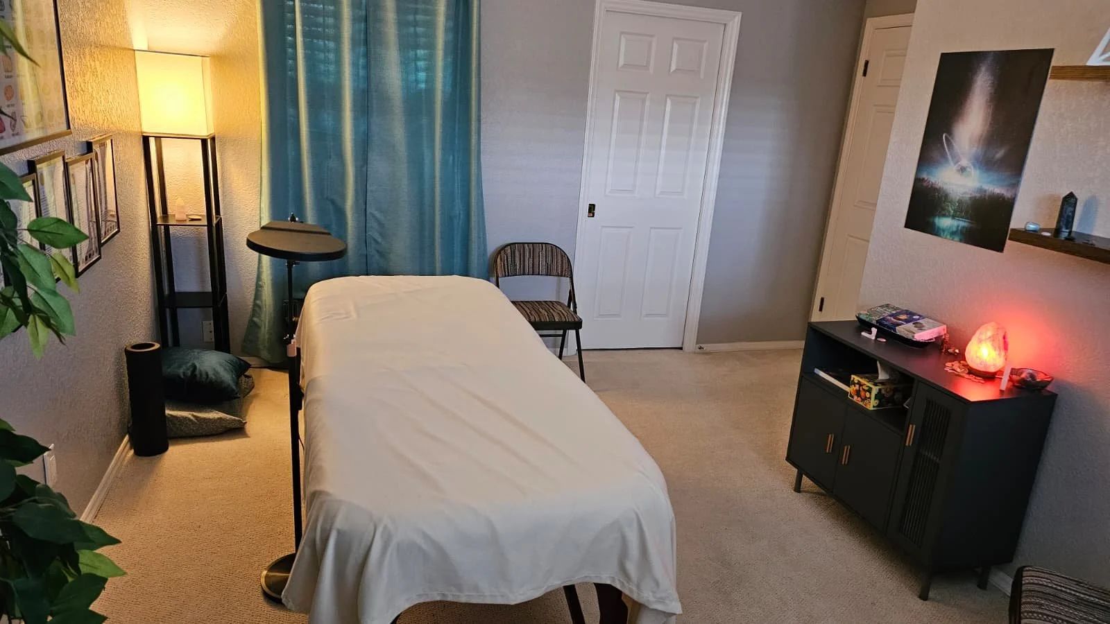 A calm session room with a padded table, blue curtains, and a softly glowing salt lamp