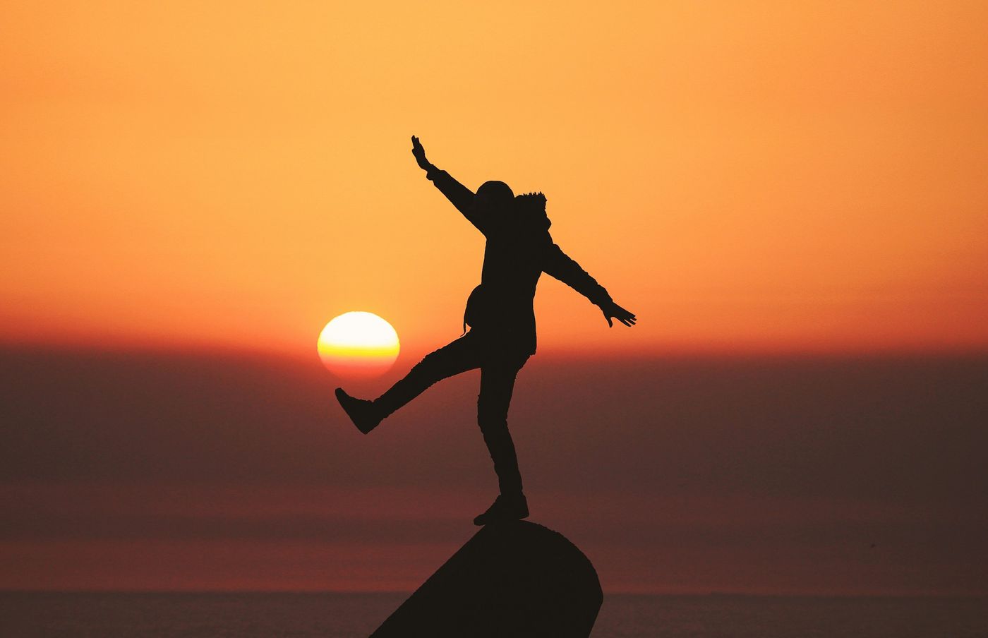 Silhouette of a person balancing on one leg against an orange sunset